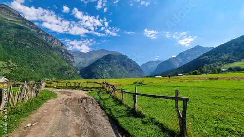 A gravelled road in high Caucasus mountains in Georgia. The road leads to a small mountain village on a steep slope. Thick clouds in the back. Lush pastures on the sides. Barren peaks. photo