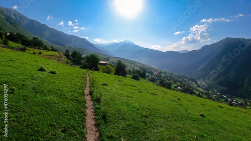 A narrow pathway in high Caucasus mountains in Georgia. There are high glaciers in the back. Thick clouds above the sharp peaks. Lush pastures on the sides. Barren peaks. Idyllic landscape. photo