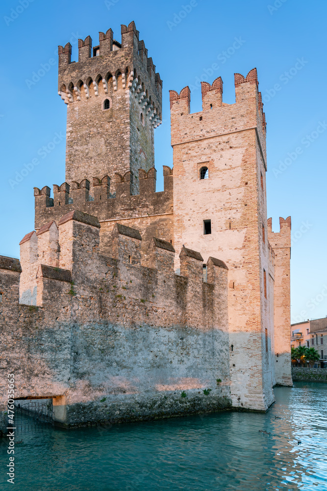 Water fortress with tall stone towers and battlement walls under clear sky in Sirmione