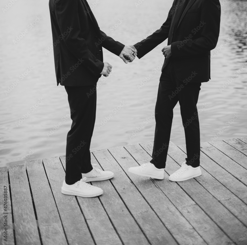 Fotka „European Gay Couple holding hands, wearing black suits, wedding day  of a same sex couple. Black and white art photography.“ ze služby Stock |  Adobe Stock