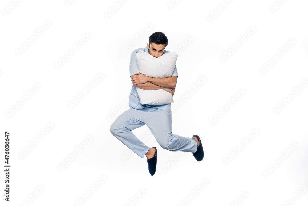 young man in pajamas levitating and hugging pillow isolated on white.