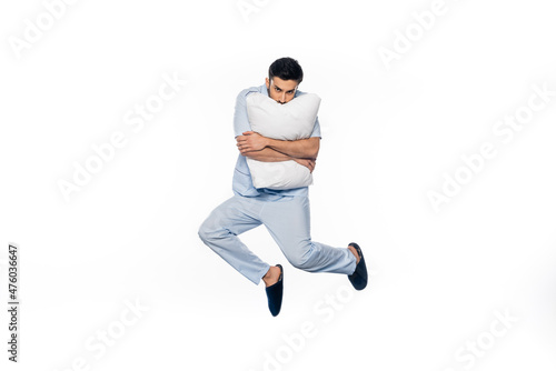 young man in pajamas levitating and hugging pillow isolated on white.