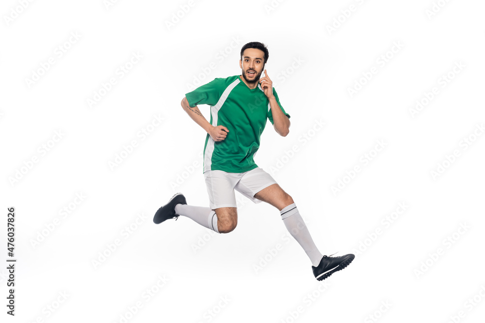 happy football player in uniform jumping while talking on smartphone isolated on white.