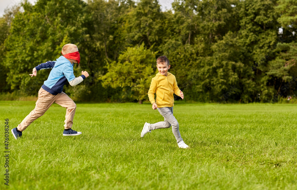 childhood, leisure and people concept - happy boys playing seek and hide game at park