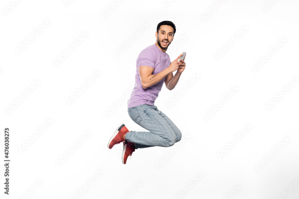 amazed man in jeans and purple t-shirt levitating while holding smartphone on white. amazed man in jeans and purple t-shirt levitating while holding smartphone on white.