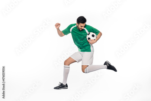 young football player in uniform jumping with soccer ball on white.