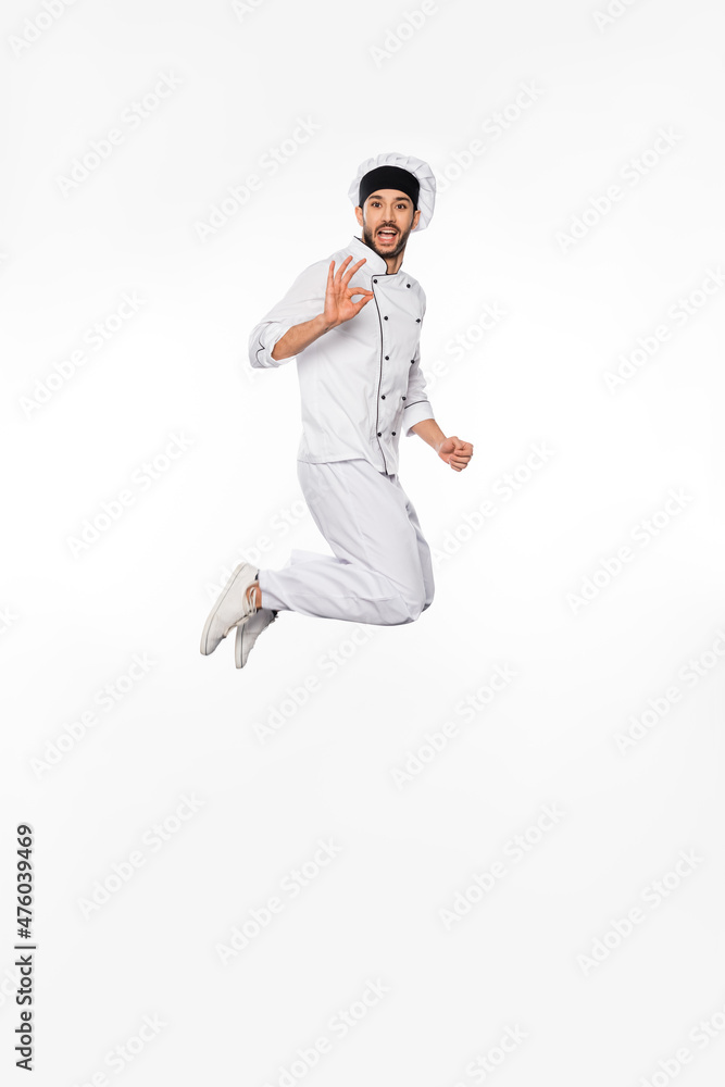 amazed chef in hat and uniform jumping and showing okay on white. amazed chef in hat and uniform jumping and showing okay on white.