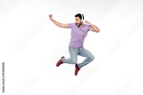 amazed and tattooed man in wireless headphones levitating on white.