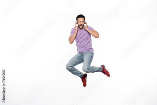 positive man in wireless headphones levitating on white.