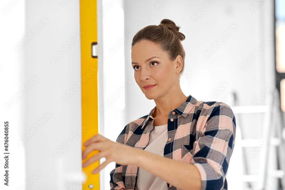 repair, construction and building concept - woman with level measuring wall at home repair, construction and building concept - woman with level measuring wall at home
