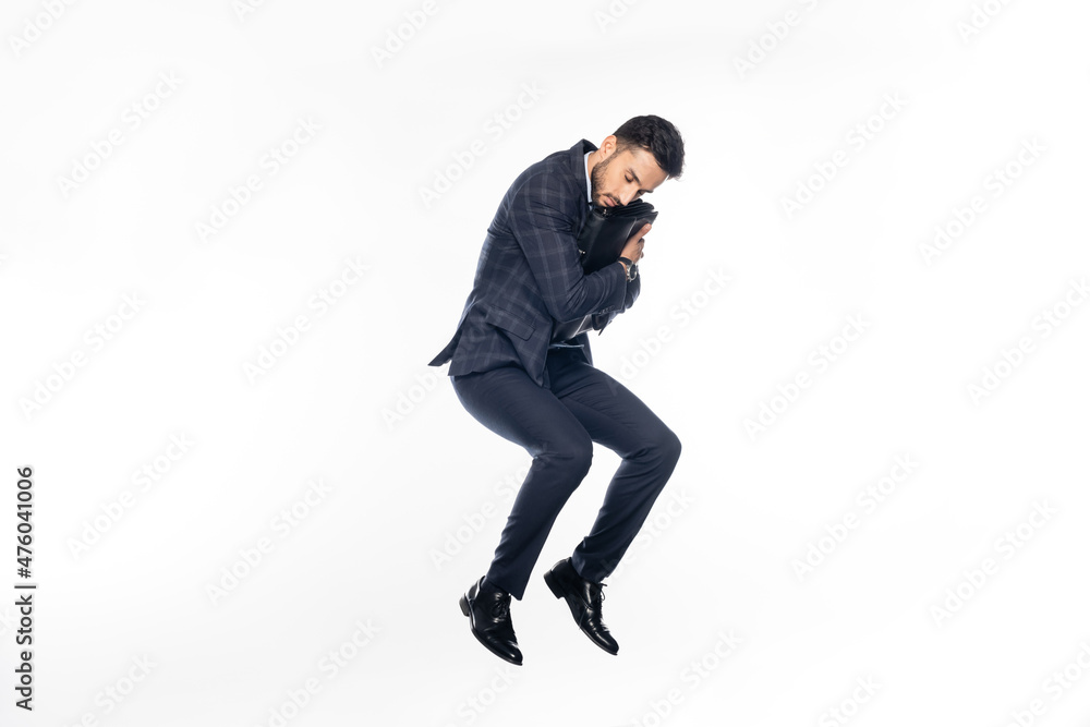 businessman in suit jumping while hugging briefcase on white.
