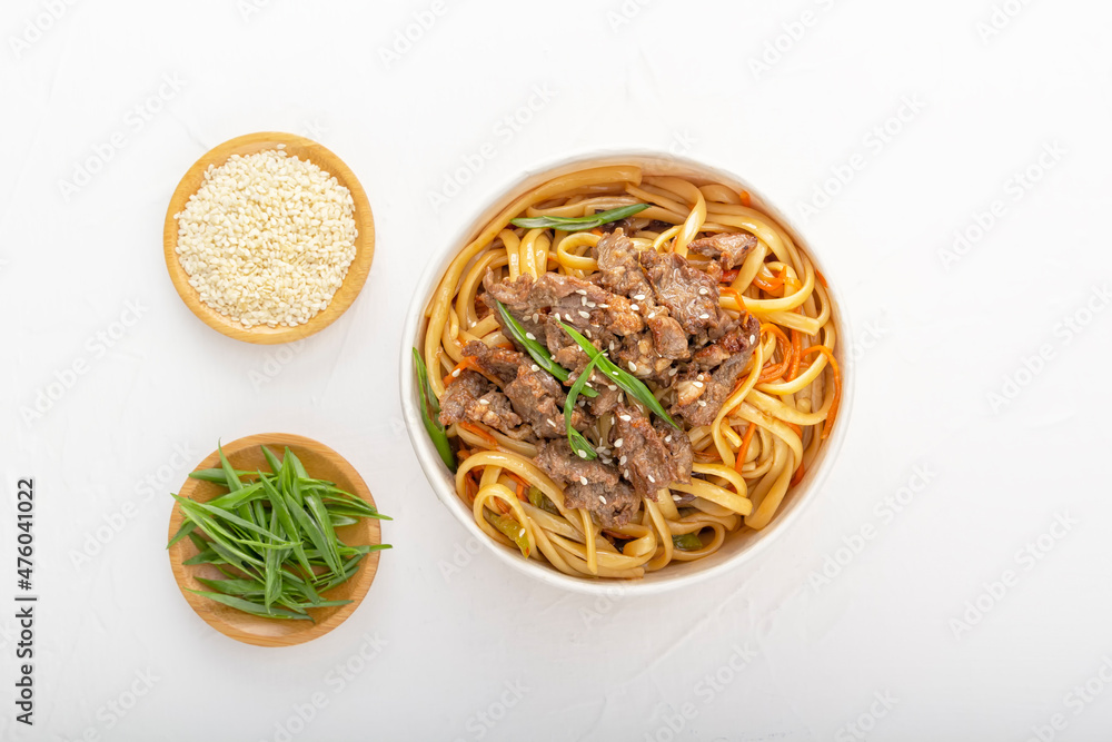 Noodles with meat, pepper, herbs and sesame seeds in a disposable paper plate on a white background. Asian street food. View from above. Noodles with meat, pepper, herbs and sesame seeds in a disposable paper plate on a white background. Asian street food. View from above.
