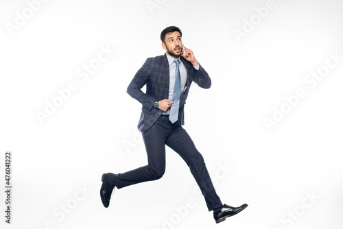 pensive businessman in suit jumping and talking on smartphone on white.