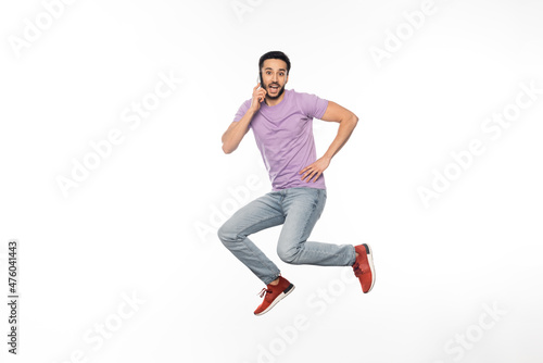 amazed man in jeans and purple t-shirt levitating while talking on cellphone on white.