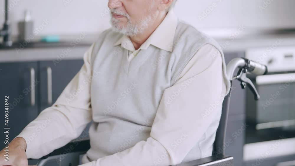 Elderly man in wheelchair rubbing painful knee after injury, joint disease Elderly man in wheelchair rubbing painful knee after injury, joint disease