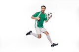 amazed football player in uniform jumping while holding soccer ball and showing thumb up on white.