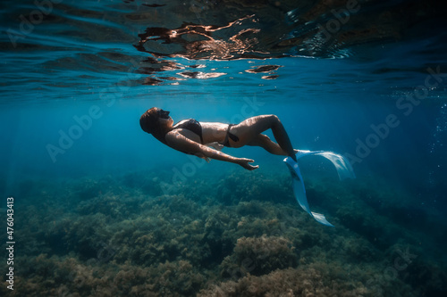 Free diver woman with fins glides underwater and surface in ocean.
