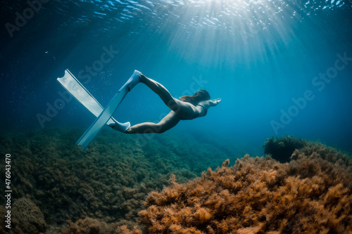 Free diver girl glides with freediving fins and sea bottom with seaweed. Freediving with woman and beautiful light in ocean