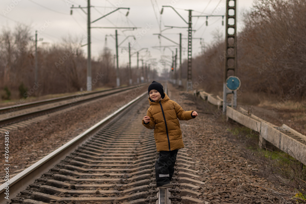 a cute boy is walking on the train tracks.he is looking at the camera and has a restless expression on his face. child safety concept on railroad rails