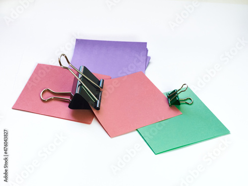Several metal paper clips and multicolored paper stickers on a white background  black and one green paper clip  office items