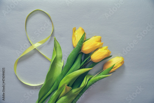 Five yellow fresh tulips on a grey background. Flowers with the number eight made of ribbon. Concept of holiday, March 8, International womans day. Card with copy space. photo