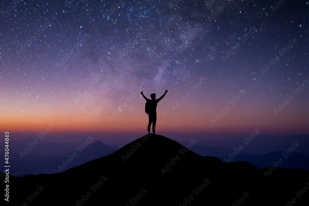 Young traveler with backpack standing and open both arm watched night sky view, star and milky way alone on top of the mountain. He enjoyed traveling and was successful when he reached the summit.