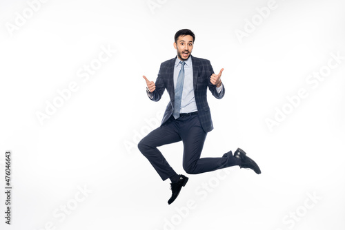 amazed businessman in suit jumping while showing thumbs up on white.