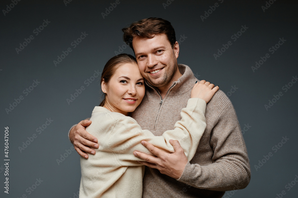Waist up portrait of adult couple embracing and looking at camera in studio against black backckground Waist up portrait of adult couple embracing and looking at camera in studio against black backckground