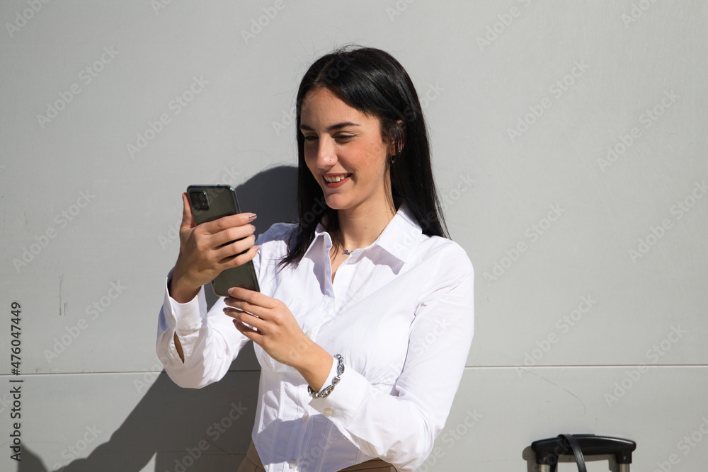 young, beautiful, dark-haired woman is consulting her mobile phone at the entrance door of the building where she works as an office worker. Concept of working woman and businesswoman. young, beautiful, dark-haired woman is consulting her mobile phone at the entrance door of the building where she works as an office worker. Concept of working woman and businesswoman.