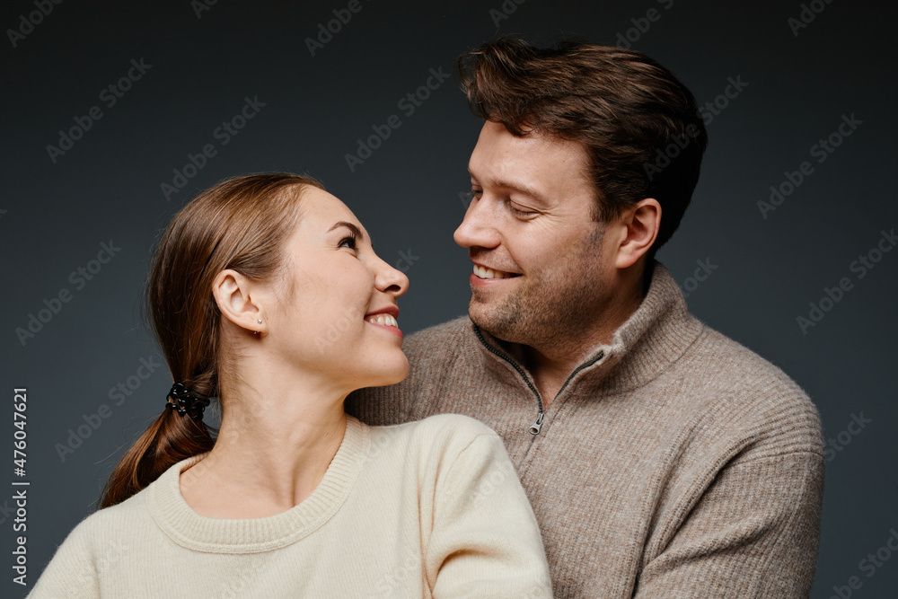 Obraz premium Portrait of happy adult couple embracing and looking at each other in studio against black backckground