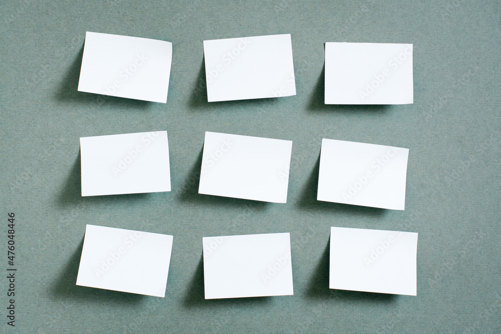 Blank small sheets of paper are arranged in rows on the green background. Green concept. Reminders and goals. Top view Blank small sheets of paper are arranged in rows on the green background. Green concept. Reminders and goals. Top view