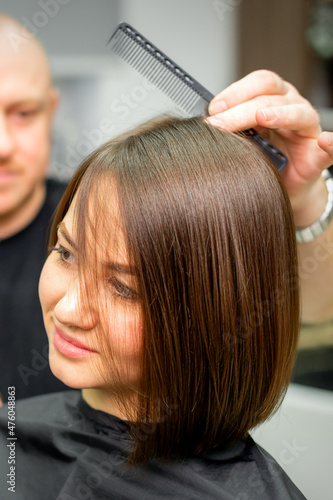 Young caucasian brunette woman having her hairstyling by a male hairdresser at a parlor