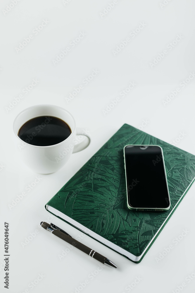 Flat lay of, cell phone, pen, and green notebook on white background with cup of coffee Flat lay of, cell phone, pen, and green notebook on white background with cup of coffee