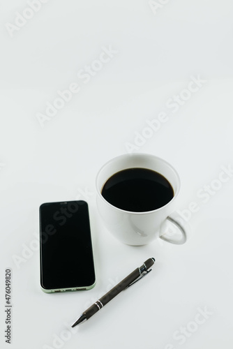 Cup of coffee with a cell phone and pen on white background