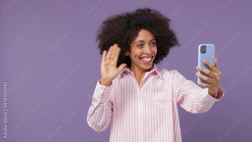 Fun young black woman 20s wears pink shirt get video call using mobile cell phone talk conducting pleasant conversation greet with hand isolated on plain pastel light purple background studio portrait Fun young black woman 20s wears pink shirt get video call using mobile cell phone talk conducting pleasant conversation greet with hand isolated on plain pastel light purple background studio portrait