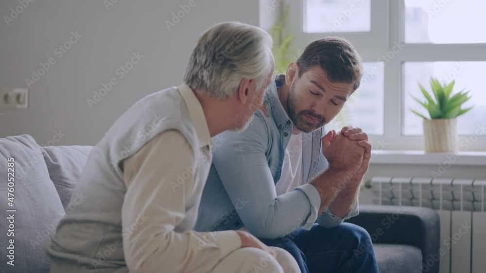 Senior father hugging, cheering up unhappy adult son sitting on couch, support Senior father hugging, cheering up unhappy adult son sitting on couch, support