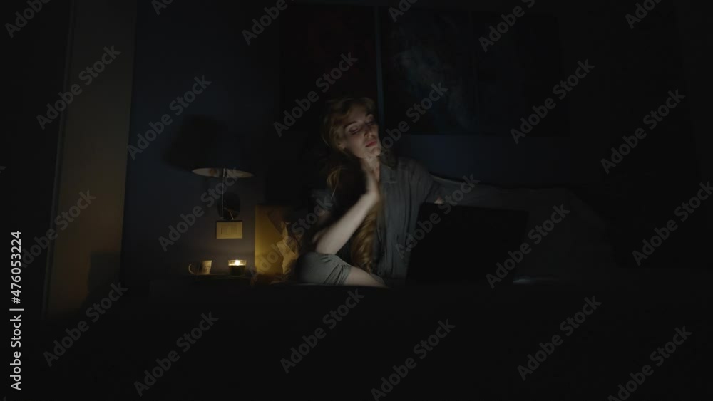 Student studying late at night in her bed at home, the woman is tired from a long day of work Student studying late at night in her bed at home, the woman is tired from a long day of work