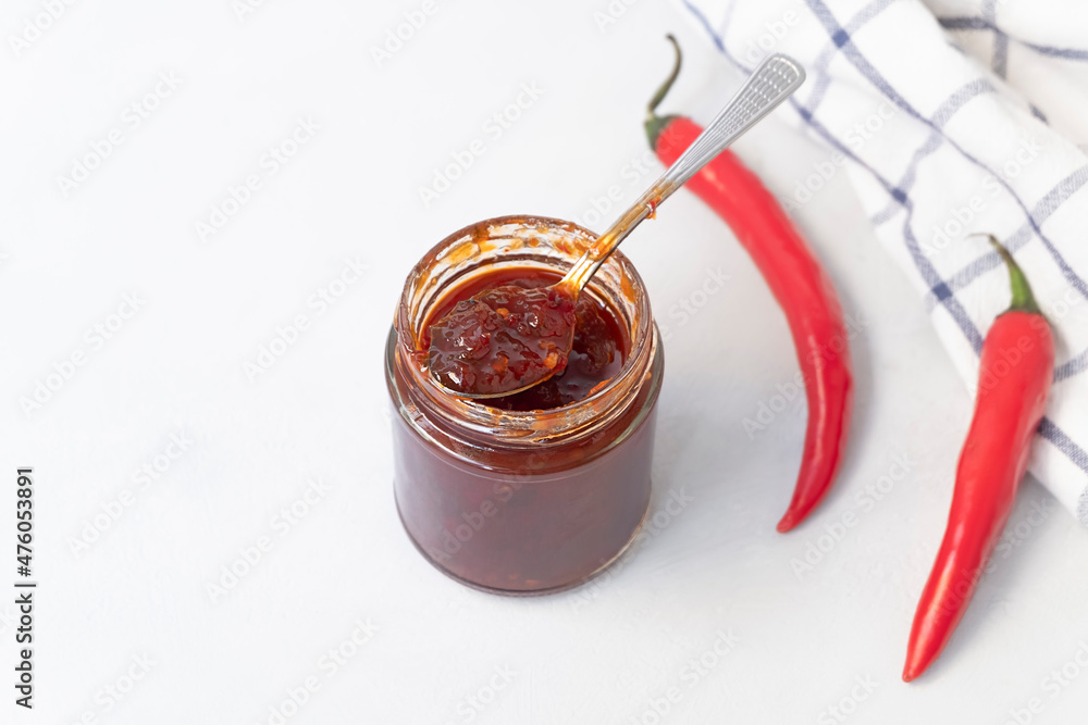 Above view of jar with sweet spicy jam made from chili pepper on neutral grey background with copy space, selective focus