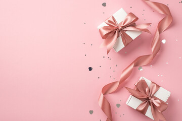 Top view photo of white gift boxes with pink bows curly ribbon silver sequins and heart shaped confetti on isolated pastel pink background with copyspace