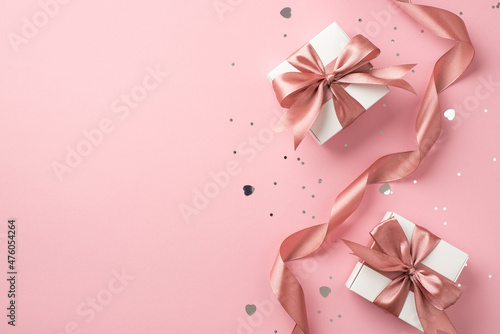Top view photo of white gift boxes with pink bows curly ribbon silver sequins and heart shaped confetti on isolated pastel pink background with copyspace photo