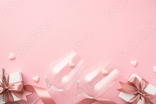 Top view photo of valentine's day decorations two wineglasses pink silk ribbon small hearts and white gift boxes with bows on isolated pastel pink background with blank space