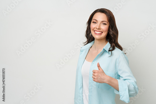 Enthusiastic motivated attractive young woman , brunette, giving a thumbs up gesture of approval and success with a beaming smile.