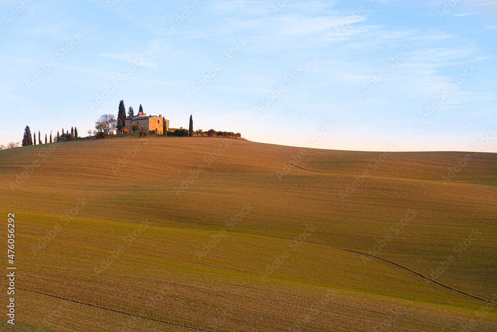 Obraz premium Hills with plowed fields in the Italian countryside in Val D'Orcia, photographed at sunset. Warm light, with a cottage and trees in the background. Relaxing landscape with lines formed by plow furrows