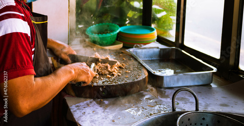 Adult male taquero cutting meat at a Mexican restaurant to prepare carnitas tacos.  photo