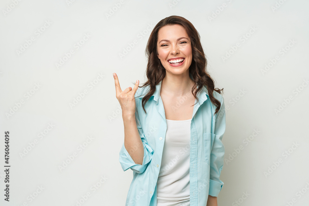 Emotive brunette woman make rock n roll sign, , yells loudly, stands over white background with empty space, feels self confident. Emotive brunette woman make rock n roll sign, , yells loudly, stands over white background with empty space, feels self confident.