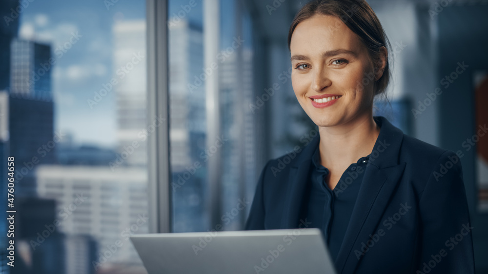 Successful Businesswoman in Stylish Dress Working on Laptop, Standing Next to Window in Big City. Confident Female CEO Analyze Financial Projects. Manager at Work Planning Marketing Campaign. Successful Businesswoman in Stylish Dress Working on Laptop, Standing Next to Window in Big City. Confident Female CEO Analyze Financial Projects. Manager at Work Planning Marketing Campaign.