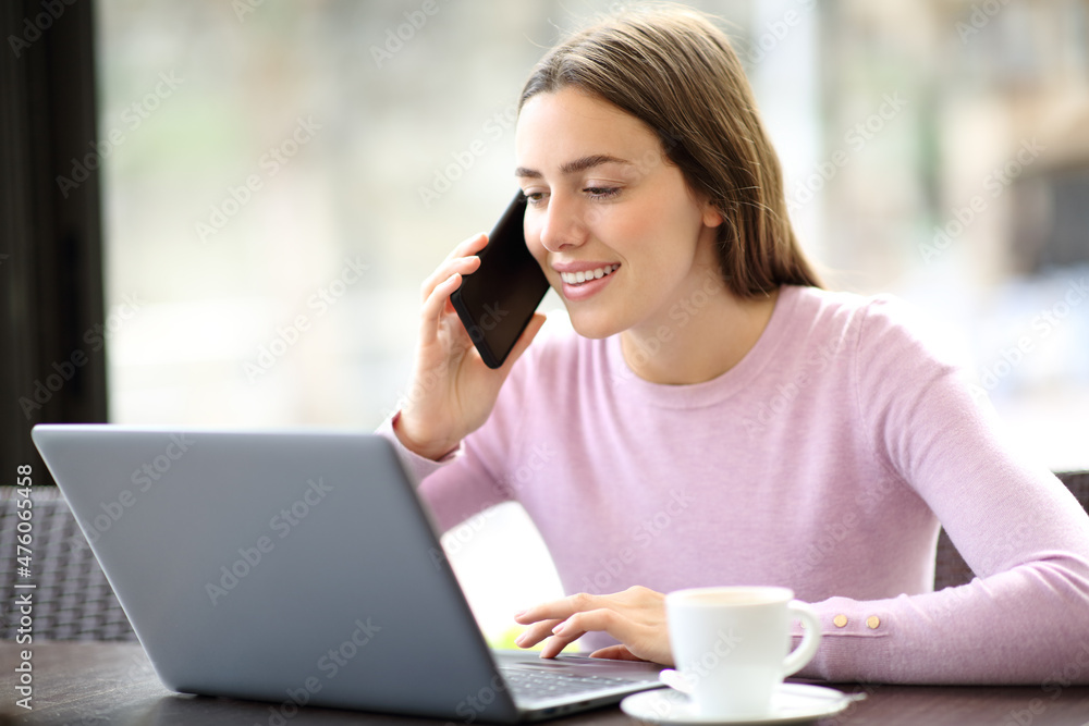 Woman in a coffee shop using laptop talking on phone Woman in a coffee shop using laptop talking on phone