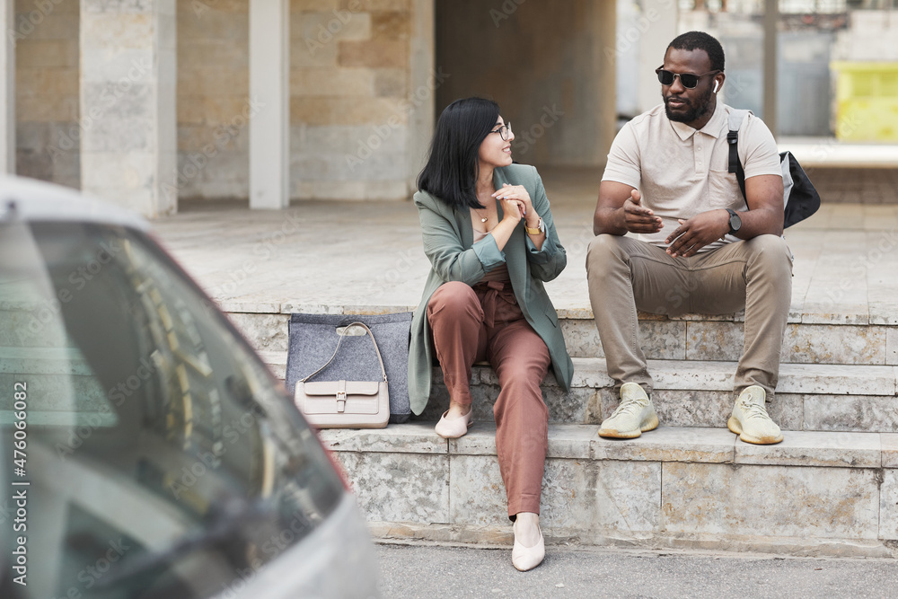 Full length portrait of two young business people chatting while sitting on steps in city, copy space Full length portrait of two young business people chatting while sitting on steps in city, copy space