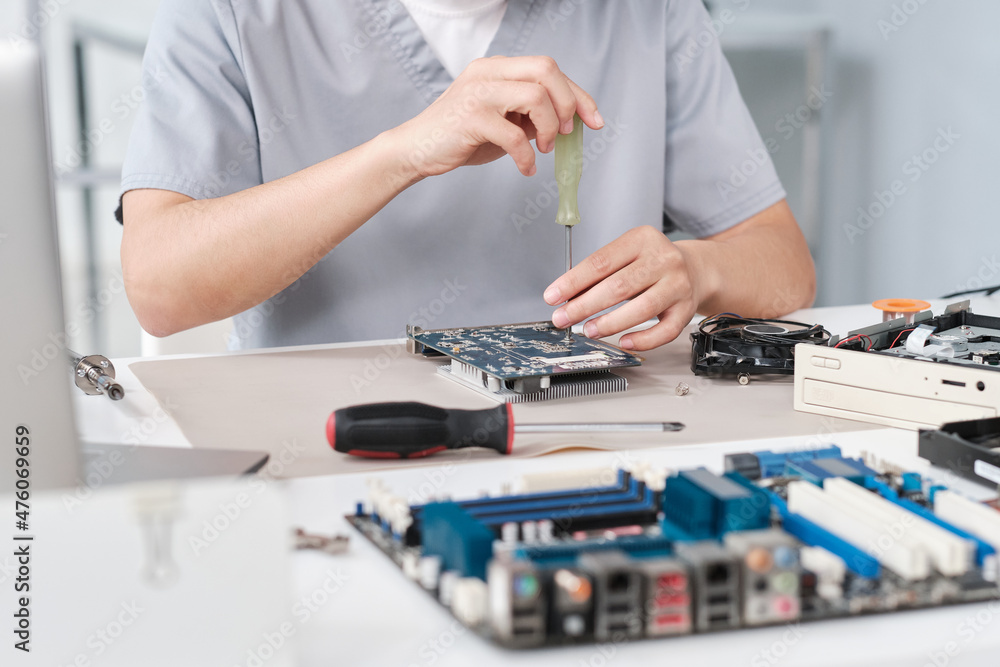 Hands of young repairperson in uniform fixing details of circuit board with screwdriver while sitting by desk in laboratory Hands of young repairperson in uniform fixing details of circuit board with screwdriver while sitting by desk in laboratory