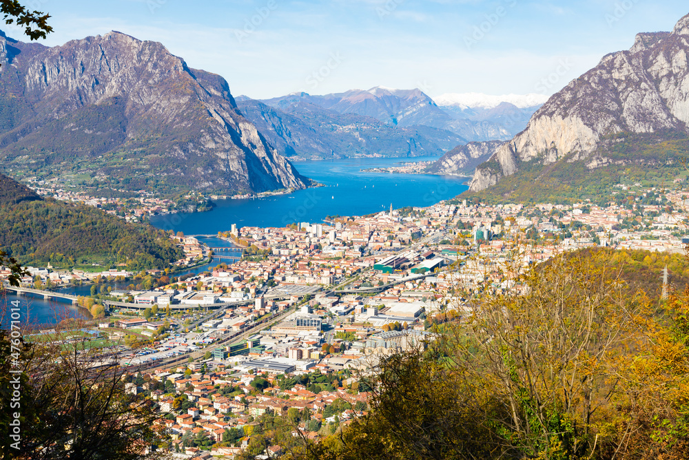 Aerial view of the city of Lecco, Italy, with the blue waters of Lake Como. Italian alps with blue sky on the background. Bushes on the foreground,